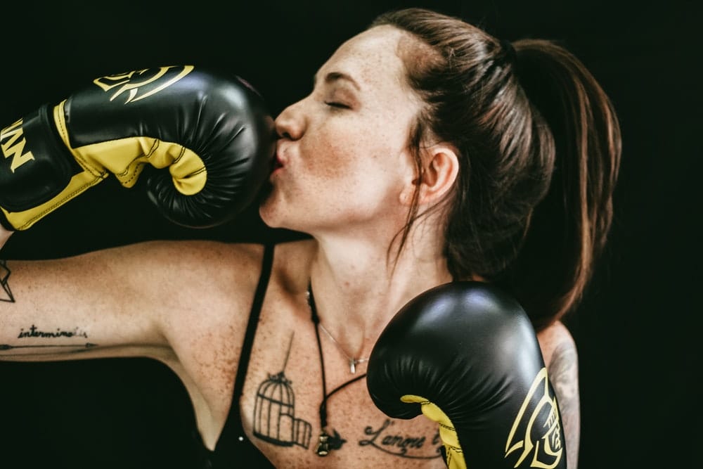 A young woman in black boxing gloves kissing one of her gloves