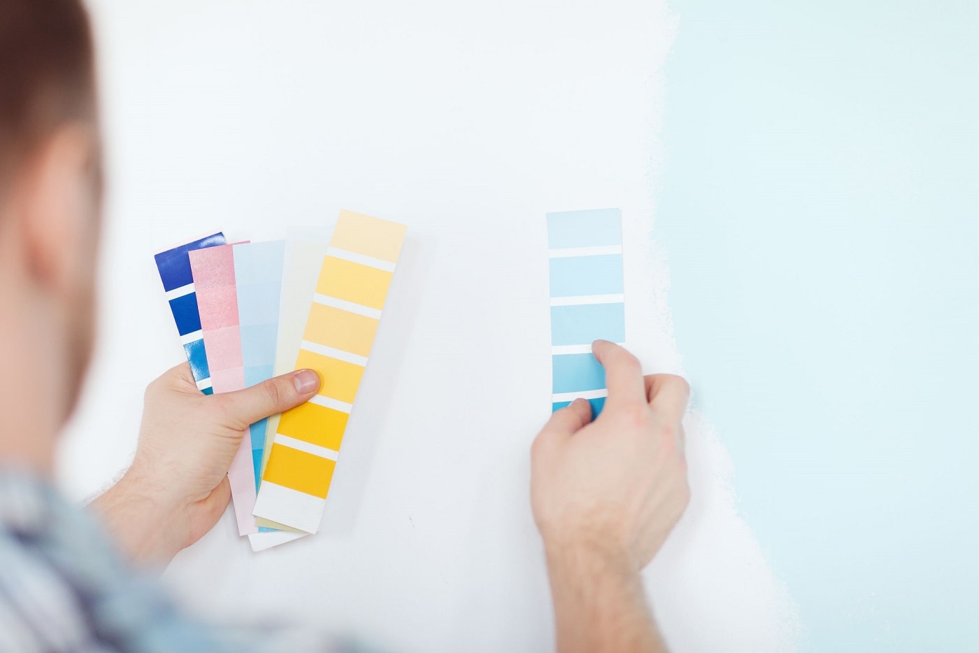 Person holding paint color swatches up against the wall
