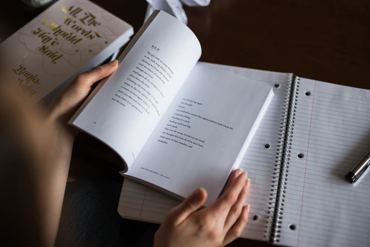 Person reading book with notepad and pen