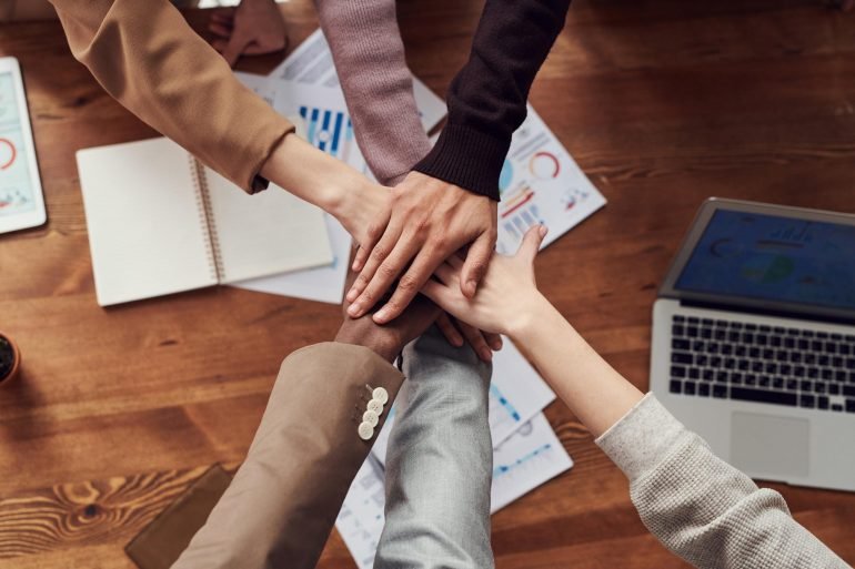 People joining hands over a wooden table and laptop