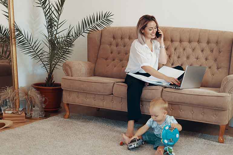 Woman working from home on sofa with child at feet