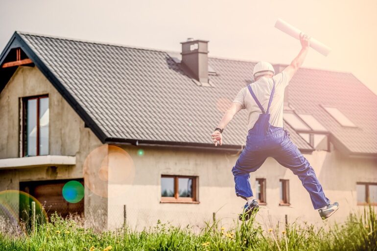 Builder holding plans and jumping for joy in front of a house