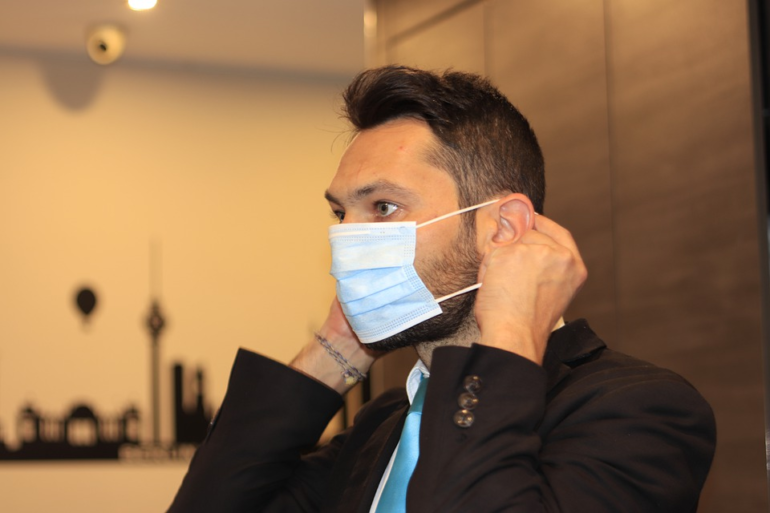 Man wearing a suit putting on a protective face mask