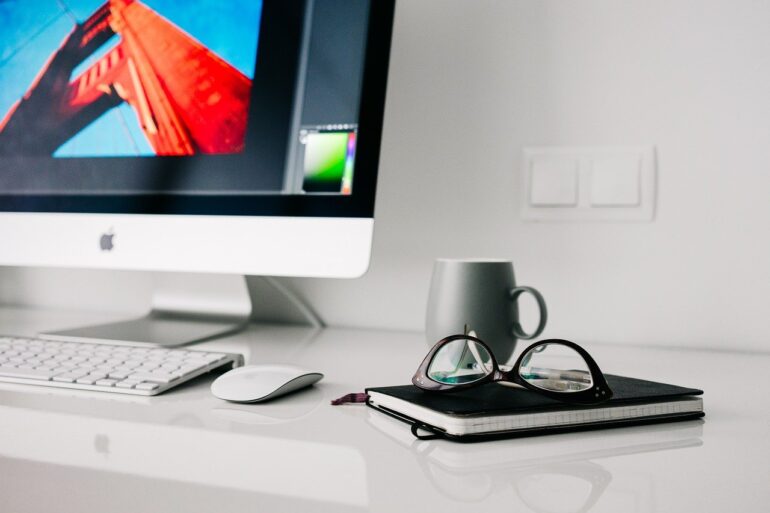 Notebook, glasses and mug by an iMac
