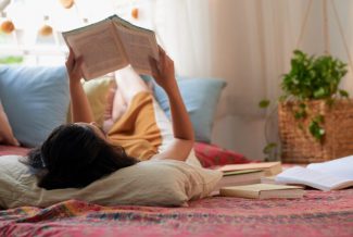 Woman laying on her back in bed reading a book
