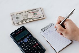 Calculator, cash and a list of bills to pay on a notepad