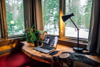 Cosy log desk in front of a window with laptop and angled lamp on the top