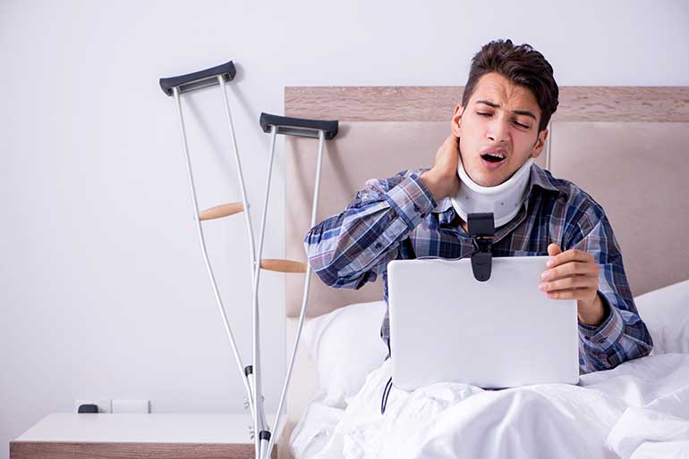 Man sitting in bed with crutches and wearing a neck brace
