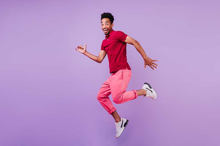 Happy looking man jumping while wearing trainers and pink tracksuit pants