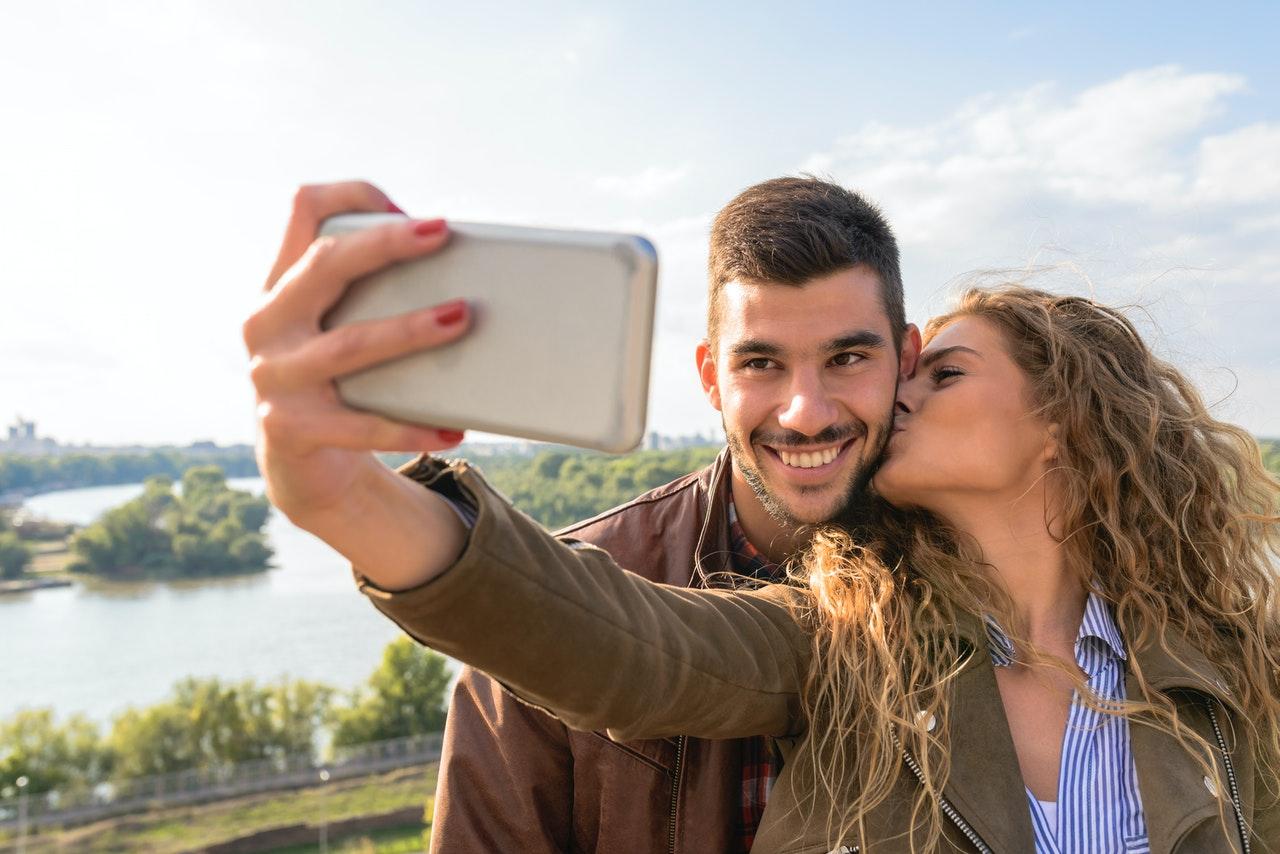 Woman kissing a man's cheek while taking a selfie