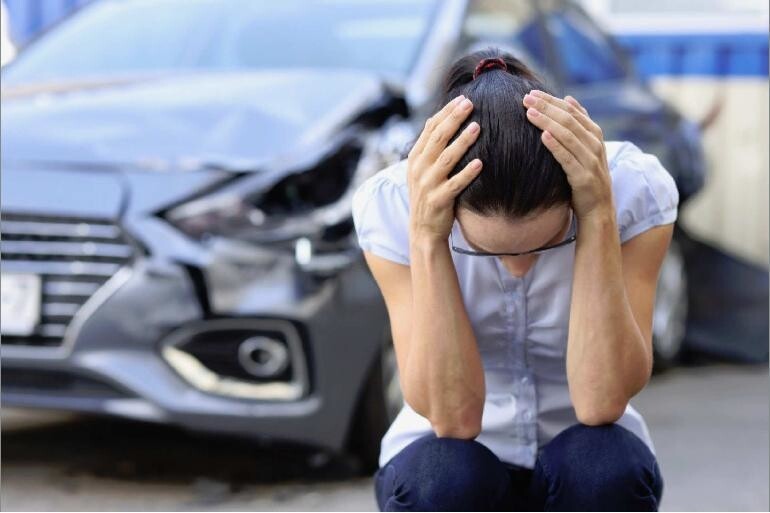 Woman holding her head in her hands in front of a damaged car