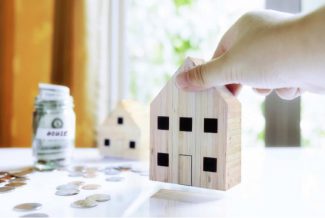 Wooden model house with a savings pot filled with money and coins on the table