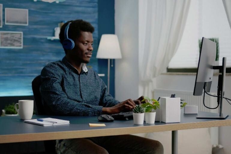 Young man using a computer in a home office while listening to headphones