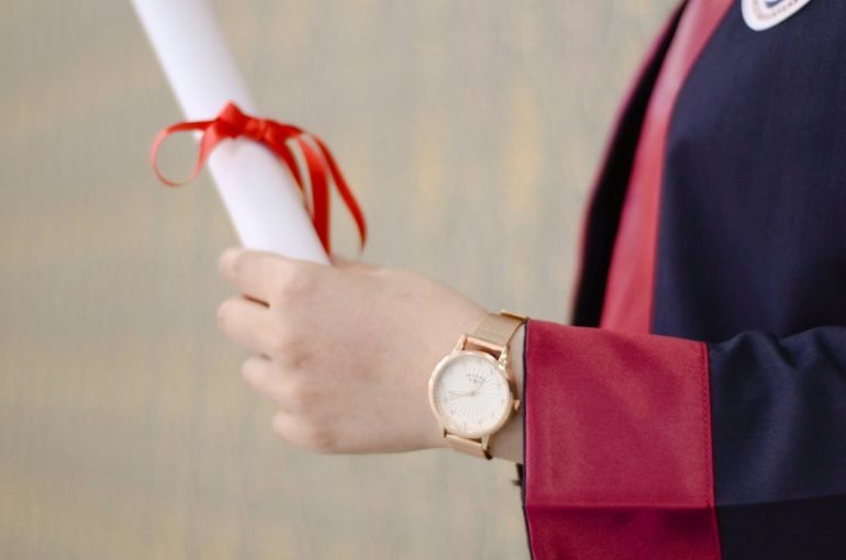 Person in graduation gown holding a certificate with a bow on it