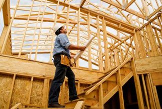 Person in safety gear looking at the wooden framework of a house