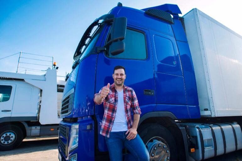 Man standing in front of a blue Freight/HGV truck while smiling and giving the thumbs up
