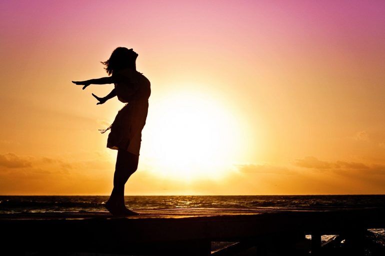 Silhouette of a woman against the sun setting over the ocean