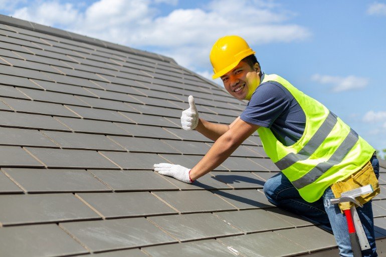 Man on a roof in safety gear with his thumbs up