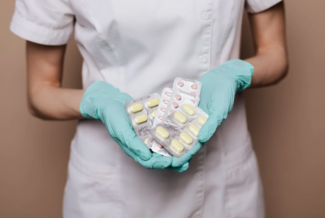 Person in medical scrubs and gloves holding packets of medication