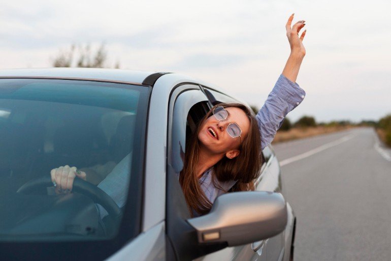 Woman driving a car with her arm and head out of the window