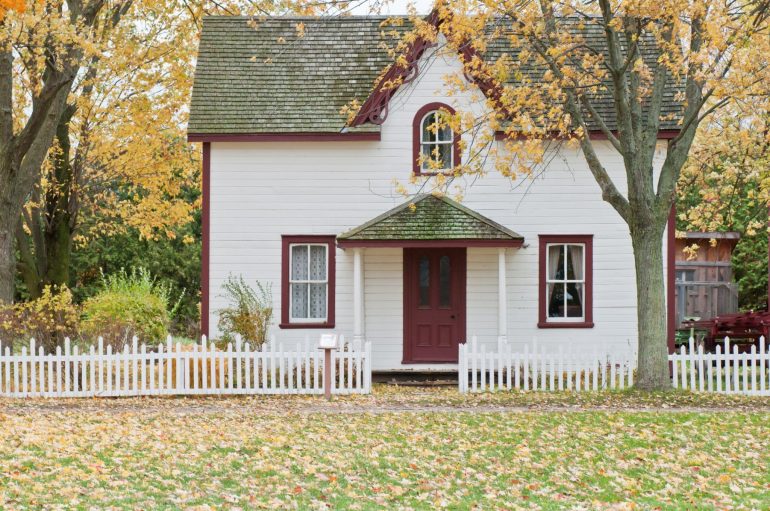 Wooden home painted white with a red trim and white picket fence