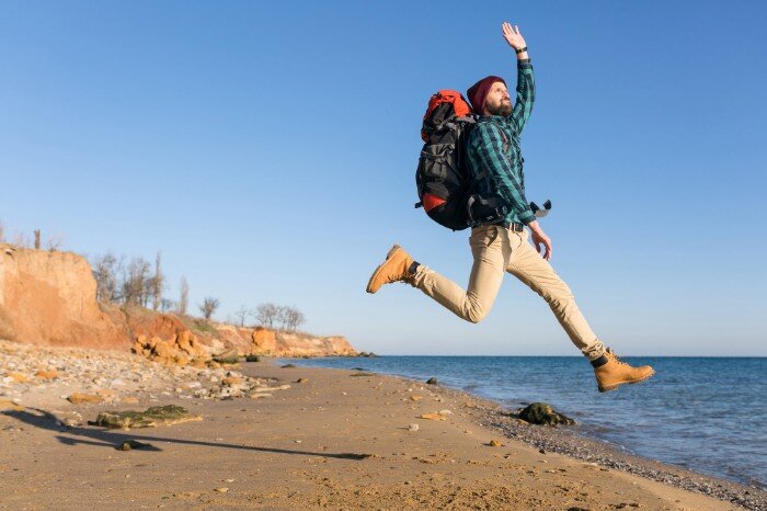 Person in hiking gear leaping in the air by a beach