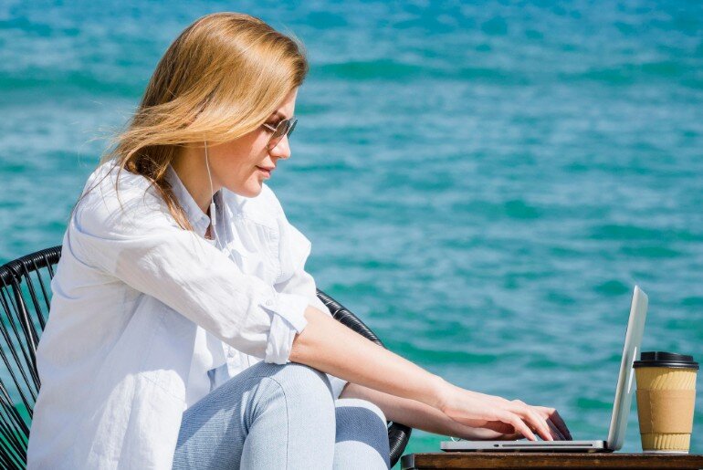 Woman sat by the ocean working on a laptop