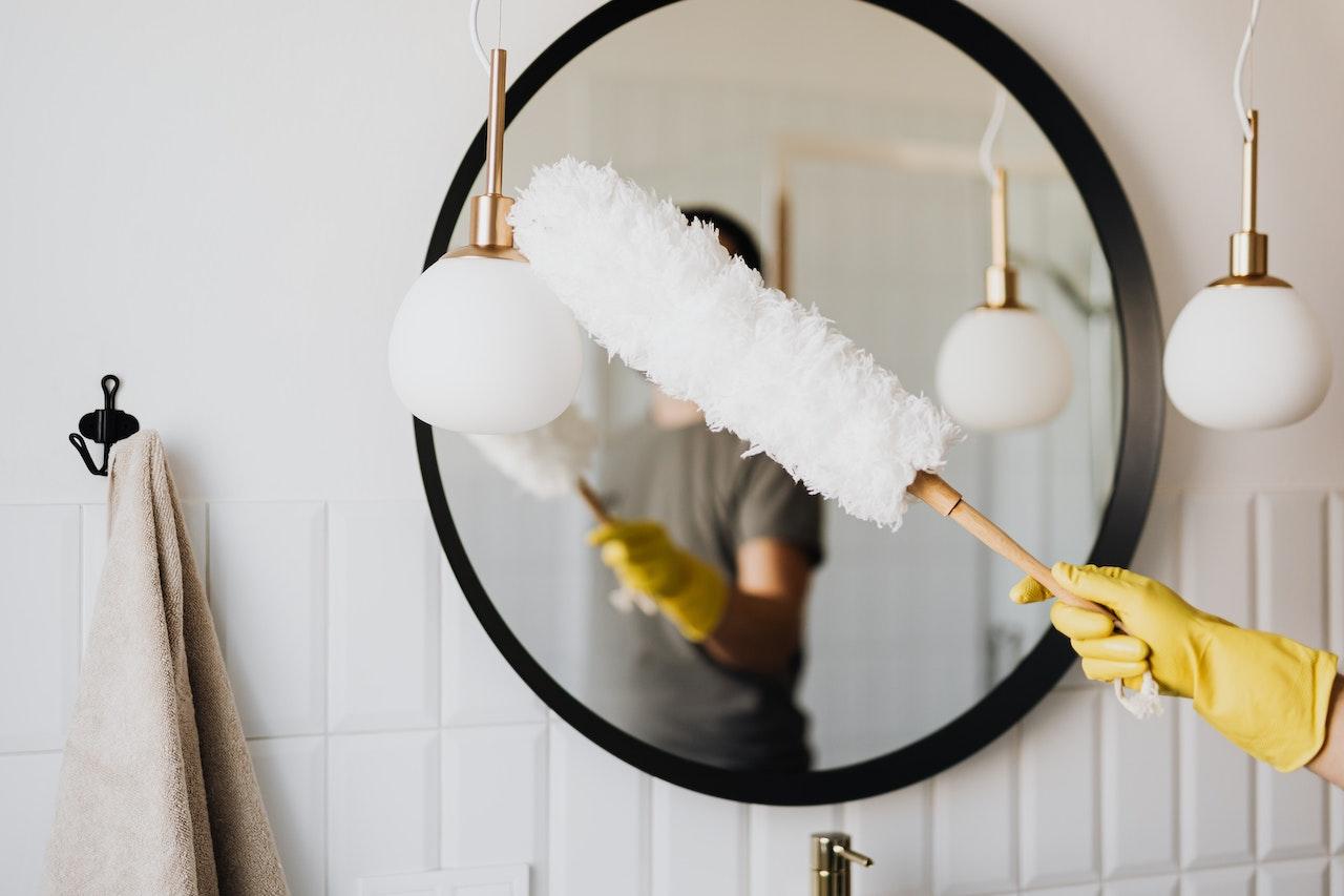 Person wearing yellow rubber gloves cleaning a mirror with a feather duster