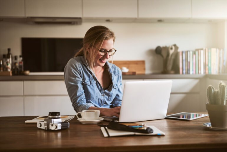 Smiling woman using a laptop at a kitchen table