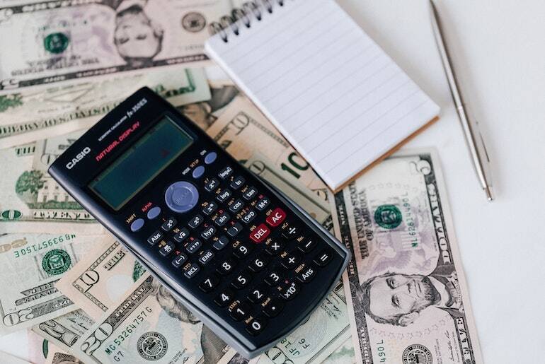 Calculator on some bank notes next to a notepad and pen