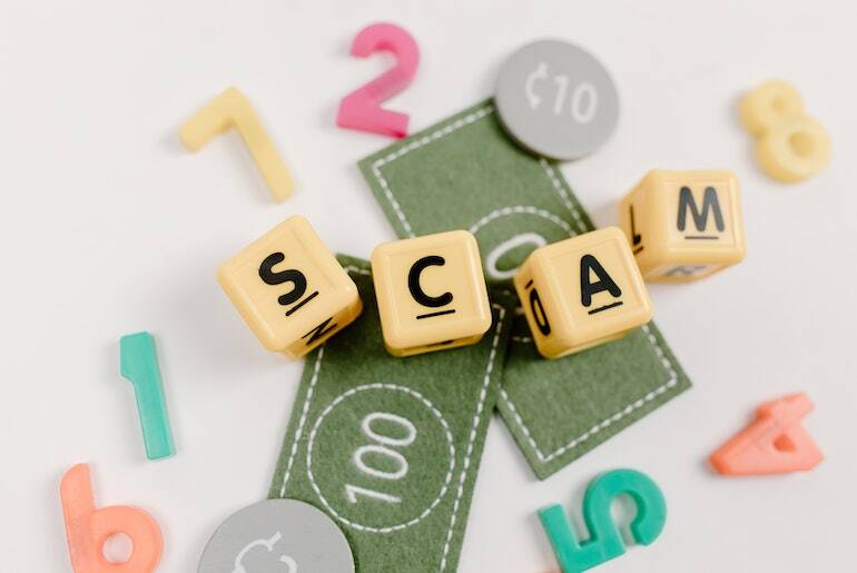 The word "Scam" spelled out in blocks on top of some toy money
