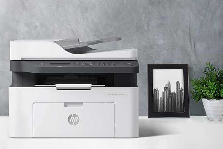 Picture of a wireless printer sat on a desk alongside a picture and a small plant