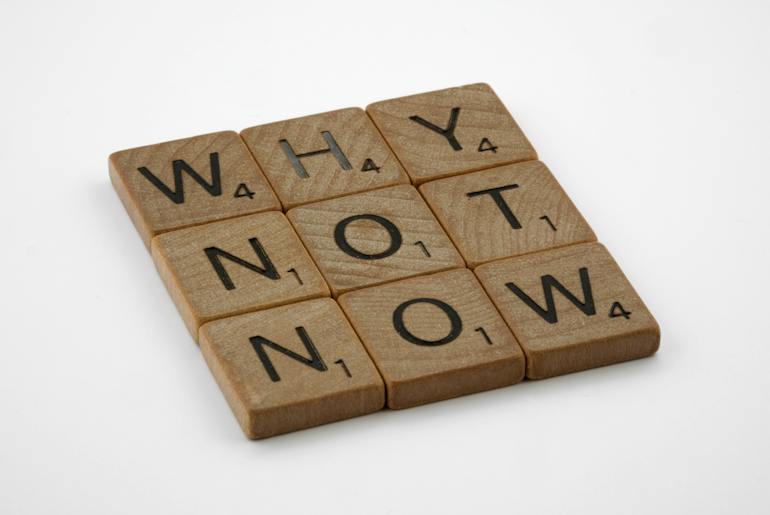 Wooden blocks saying "Why Not Now" on a white surface