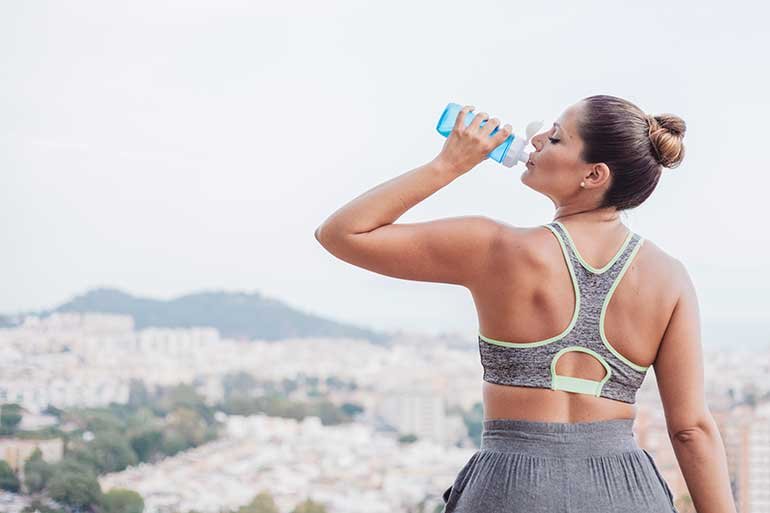 A woman drinking a bottle of water while out on a hike