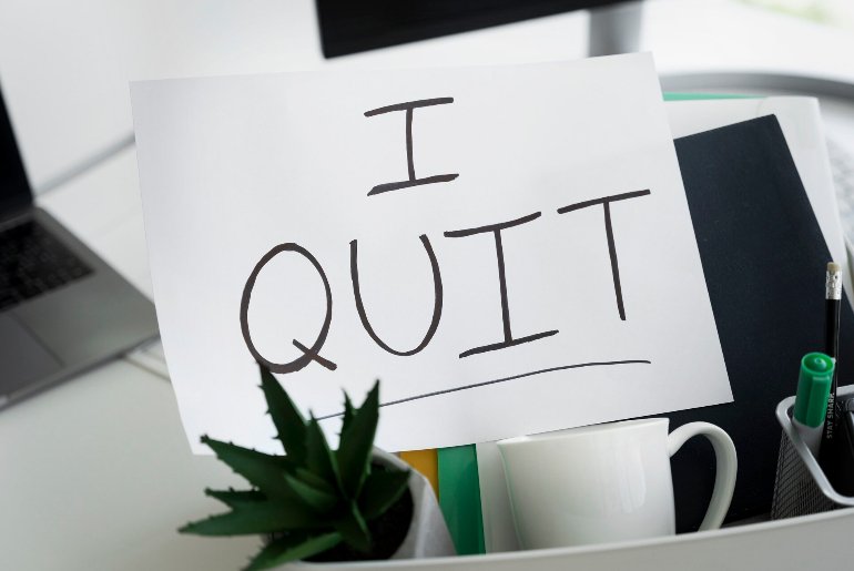 A sign that reads “I quit” propped on a box containing personal items from an office desk